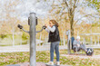 © Pepe Quilez - Happy Caucasian girl using an apparatus in the exercise park for seniors. Concept of a fitness park. Unrecognizable elderly lady in the background.