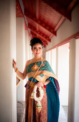 Portrait of an Asian woman in a beautiful Thai dress holding a flower wreath in a Thai Buddhist temple