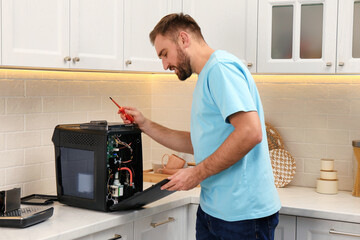 Canvas Print - Man with screwdriver fixing coffee machine at table in kitchen