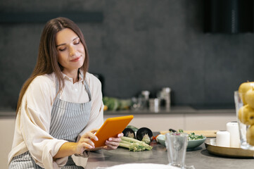 Poster - Young woman sitting in the kitchen and looking thoughtful