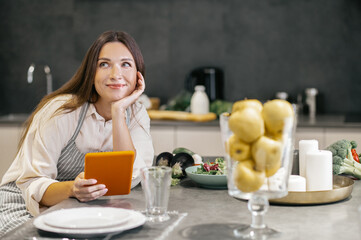 Poster - Young woman sitting in the kitchen and looking thoughtful