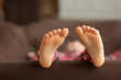 © Maria - close up child bare feet. Kid in red christmas pajamas lies on sofa