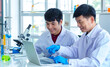 © Bangkok Click Studio - Asian professional mature male scientist teacher in white lab coat and rubber gloves sit smiling teaching science student using microscope and record analysis data in laptop computer in laboratory