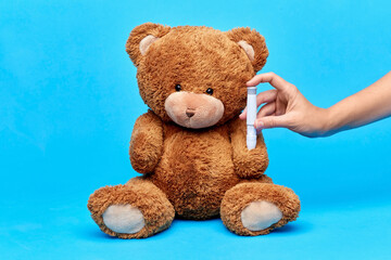 Wall Mural - medicine, healthcare and diabetes concept - hand with insulin pen making injection to teddy bear toy over blue background