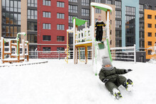 Children Ride On A Swing In The Yard In Winter. Snowy Playground