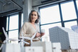 © LIGHTFIELD STUDIOS - Grey haired businesswoman holding coffee cup and looking at models of buildings in office.