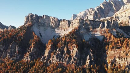 Wall Mural - Aerial flight over the Pomagagnon mountain group. Hight mountains with rocks covered by orange larches glowing by sunset light. Tre Croci Pass, Cortina D'Ampezzo, South Tyrol, Italy. UHD 4k video