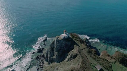 Wall Mural - Aerial panoramic view of white lighthouse on the rocky cliff at seaside. Waves are crashing to the coast. Beautiful seascape.