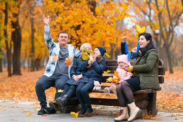 portrait of a family with children in an autumn city park - happy people sitting together on a wooden bench, posing against a background of beautiful yellow leaves