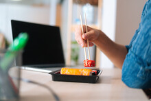 Close-up Hands Of Unrecognizable Young Business Man Holding Sushi With Chopsticks Sitting At Desk With Laptop Computer In Home Office. Closeup Of Male Employee Enjoying Sushi At Workplace
