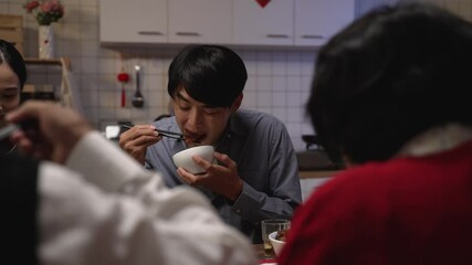 Wall Mural - selective focus of hungry asian adult male father reaching for delicious food and burning his mouth while eating reunion dinner with family on chinese lunar new year's eve at home