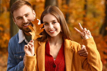 Wall Mural - Beautiful couple with autumn leaf showing victory gesture in park