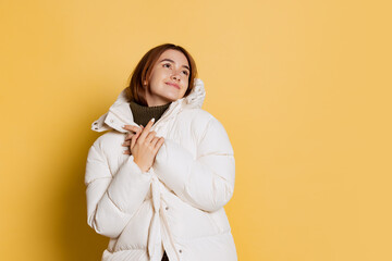 Portrait of young happy girl, student wearing warm winter coat isolated on yellow studio background.