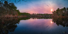 Sunrise Over The Pine Tree Forest And Glacial Kettle Pond On Cape Cod. Blue Sky, Pink And Purple Clouds Reflected On The Tranquil Water.