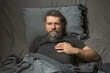 © Olga - a gray-haired young man with a beard is lying in bed and holding his chest in the heart area with his hand