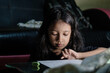 © Fajri Hidayat - Little Asian girl with long hair is writing in pencil on a table at home, on a dark background. Kid doing homework.