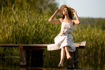 Young woman relaxing on the wooden pier at the calm lake