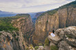 Tourist woman in white dress sitting on the edge of a cliff against the backdrop of a gorge. Amazing Tazi Canyon ,Bilgelik Vadisi in Manavgat, Antalya, Turkey. Greyhound Canyon, Wisdom Valley.