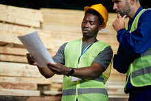 African American Warehouse Worker And His Foreman Cooperate  While Analysing Distribution Plans At Wood Department.