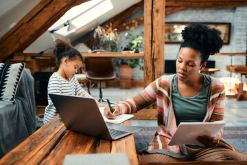 Wall Mural - Black working mother takes notes while analysing business reports at home.