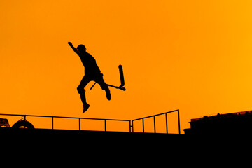 Wall Mural - Unrecognizable teenage boy silhouette showing high jump tricks on scooter against orange sunsetwarm sky at skatepark. Sport, extreme, freestyle, outdoor activity concept