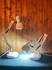 Two electric lamps on a table against a wooden wall