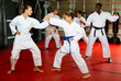 © JackF - Man and women in kimono sparring together in gym during group karate training. African-american man trainer standing nearby and observing..