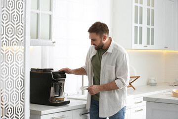 Wall Mural - Young man preparing fresh aromatic coffee with modern machine in kitchen