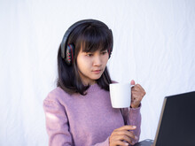Woman Wearing Headphones And Drinking Coffee In White Cup With Blur Tablet On White Background. Lifestyle Vacation In Holidays At Home. Authentic Slim Fit, Black Hair And Skin Tan Asian Thailand.