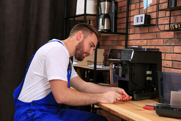 Wall Mural - Repairman with screwdriver fixing coffee machine at table indoors