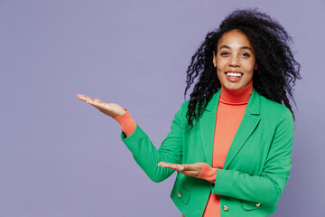 Wall Mural - Promoter fun excited young black curly woman 20s years old wear green shirt pointing aside on empty palm with copy space place mock up isolated on plain pastel light violet background studio portrait