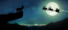 Silhouette Of Reindeer Standing On The Cliff To See Santa Claus Flying On Their Reindeer Over The Full Moon At Night Christmas.