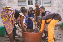 Group Of Young Black African Children Having Fun Playing Around With Fresh Water On A Public Faucet