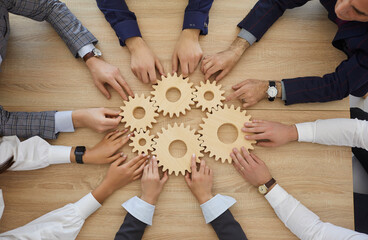 Top view of hands of business people stacking wooden gears next to each other which symbolizes development, teamwork and success. Concept of business cooperation and the corporate community. Close up.