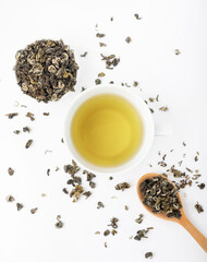 White mug with green tea on a white background. Tea leaves and a wooden spoon.