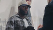 © Framestock - Positive African American male artisan in checkered shirt and cap talking then smiling and shaking hand of customer during meeting in creative workshop
