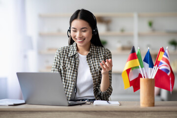 Happy asian lady using laptop and headset, learning foreign language