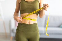 Cropped View Of Slim Indian Woman Measuring Her Waist With Tape Measure At Home, Closeup