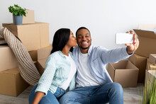 Loving Black Spouses Moving To Their Own Home, Taking Selfie Among Carton Boxes, Wife Kissing Husband In Cheek
