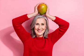 Sticker - Portrait of attractive cheerful grey-haired woman holding mango on head having fun isolated over pink pastel color background