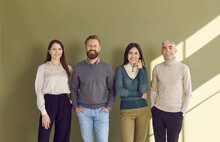 Group Portrait Of Four Happy People In Smart Casual Outfits Posing Against Green Studio Background. Team Of 4 Confident Business Men And Women Standing By Office Wall, Smiling And Looking At Camera