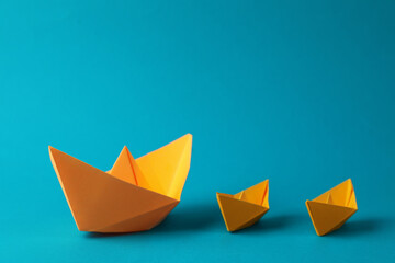 Many handmade orange paper boats on light blue background. Origami art