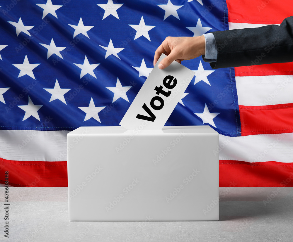 Hand placing ballot in ballot box with American flag background