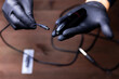 the hands of a permanent makeup artist in black medical gloves inserts a power cord into a tattoo machine against the background of a wooden table
