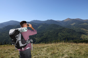 Poster - Tourist with hiking equipment looking through binoculars in mountains, back view