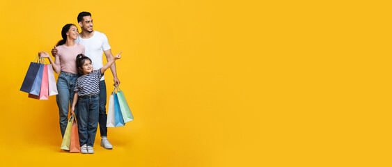 family shopping. arab parents holding shopper bags, little girl pointing aside