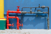 Red Fire Pipes In A City Street , Singapore . Plumbing Water Pipes Close Up Near Blue Wall