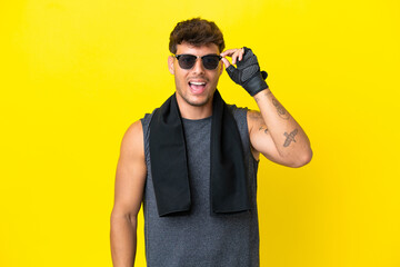 Wall Mural - Young sport caucasian man with towel isolated on yellow background with glasses and surprised