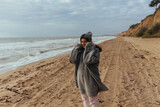 Fototapeta Kosmos - Young woman on cold autumn seashore posing at camera
