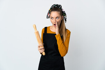 Wall Mural - Young Lithuanian woman holding a rolling pin isolated on white background whispering something with surprise gesture while looking to the side